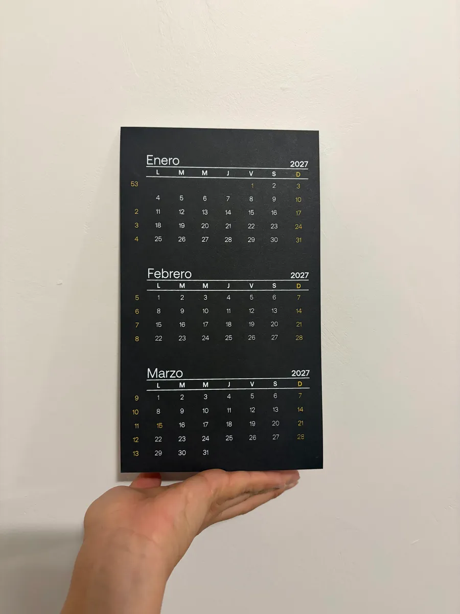 Mano sosteniendo un calendario 2027 negro con enero, febrero y marzo impresos