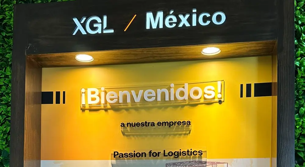 Vitrina luminosa de bienvenida de XGL en un muro verde, con letras de acrílico sobre un fondo amarillo impreso